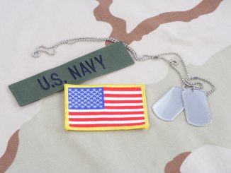 US NAVY branch tape with dog tags and flag patch on desert camouflage uniform background