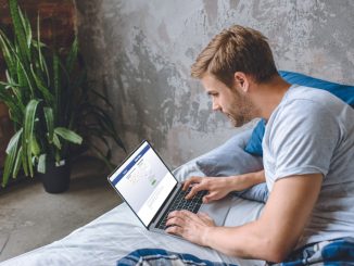 young man in bed using laptop with facebook on screen