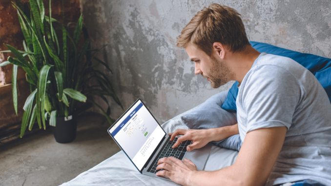 young man in bed using laptop with facebook on screen