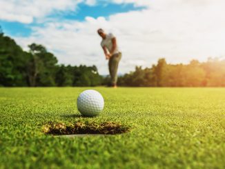 golf player putting golf ball into hole with sunshine