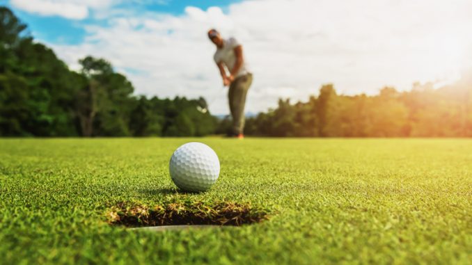 golf player putting golf ball into hole with sunshine