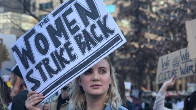 Blonde Woman holding War style protest sign representing the Me Too movement