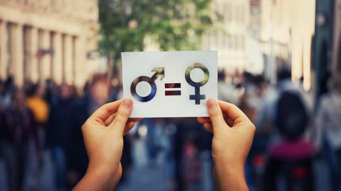 Gender equality concept as woman hands holding a white paper sheet with male and female symbol over a crowded city street background.