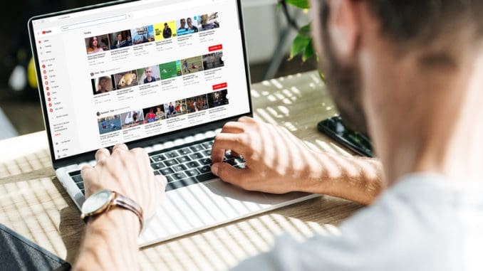 back view of man using laptop with youtube website on screen